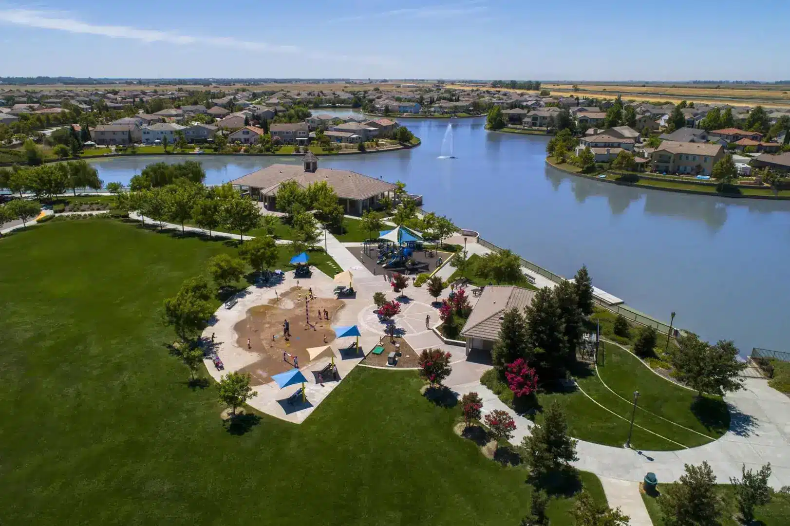 Aerial view of Bridgeway Lakes Community Park in West Sacramento, CA featuring splash pad, green lawns, and scenic lake