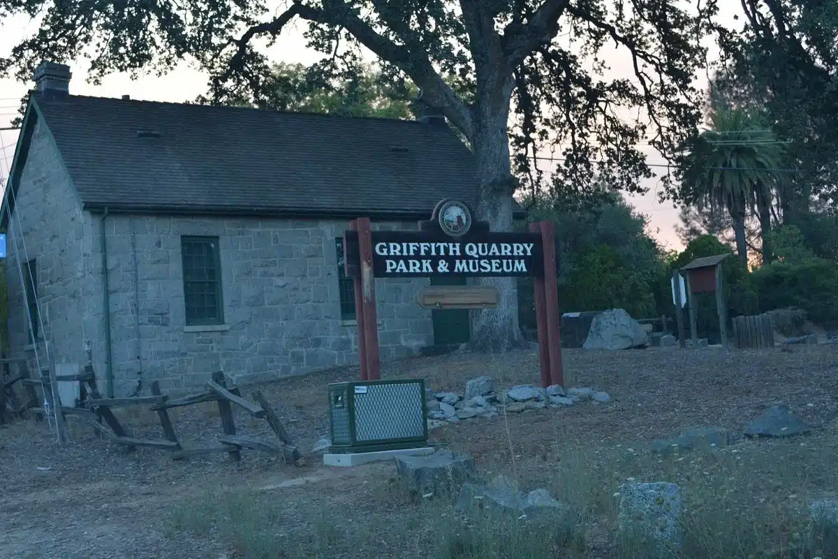 The rustic entrance sign for Griffith Quarry Park & Museum in Penryn, CA, with the historic stone museum building in the background.