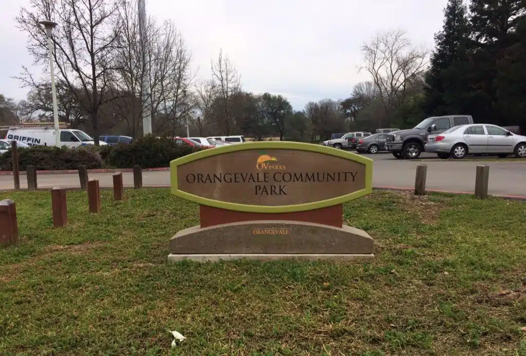 Entrance sign at Orangevale Community Park in Orangevale, CA with parking and trees in the background